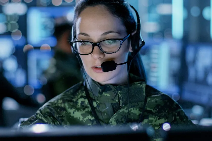 A Canadian Armed Forces operator in a monitoring centre working at a wall of screens.
